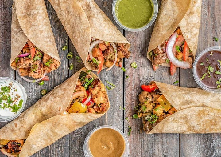 Five burritos on a table with sauces